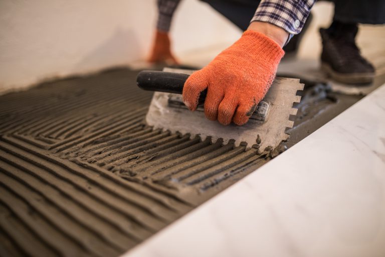 Laying Ceramic Tiles. Troweling mortar onto a concrete floor in preparation for laying white floor tile